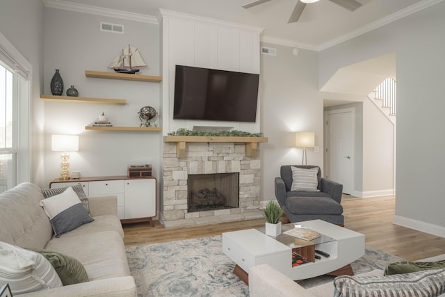 living room with crown molding, visible vents, a stone fireplace, and light wood finished floors