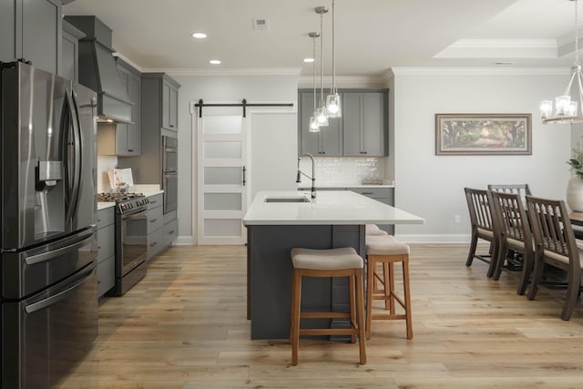 kitchen featuring custom exhaust hood, ornamental molding, a barn door, appliances with stainless steel finishes, and a sink