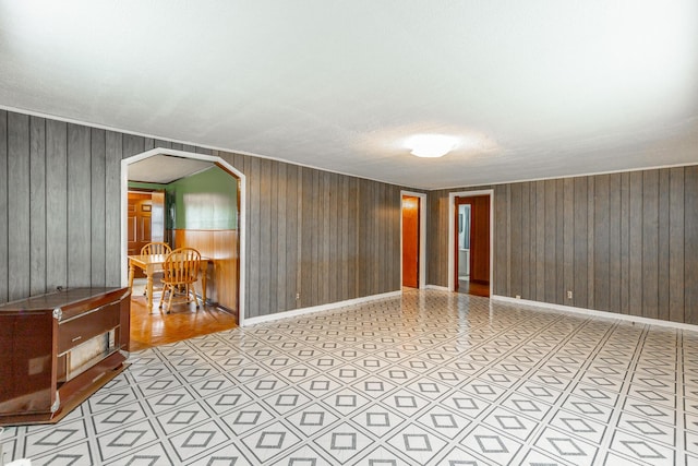 empty room featuring arched walkways, baseboards, wood walls, and a textured ceiling