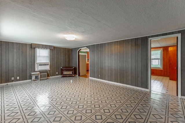 empty room featuring arched walkways, baseboards, and wood walls