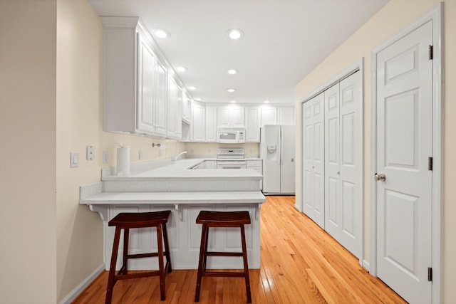 kitchen with a sink, light countertops, white appliances, a peninsula, and light wood-style flooring