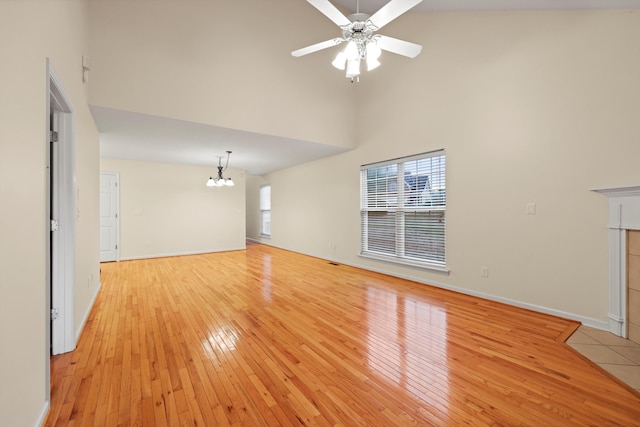 unfurnished living room featuring light wood-style flooring, baseboards, a towering ceiling, and ceiling fan with notable chandelier