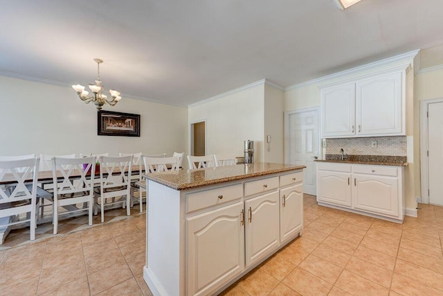 kitchen featuring an inviting chandelier, light tile patterned floors, a center island, crown molding, and decorative backsplash