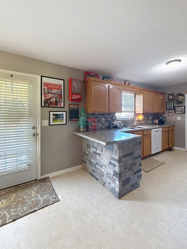 kitchen featuring light tile patterned floors, a peninsula, a sink, white dishwasher, and decorative backsplash