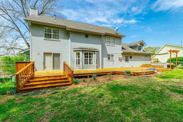 rear view of house featuring a yard, a shingled roof, a deck, and a chimney