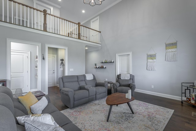 living area with a high ceiling, an inviting chandelier, wood finished floors, crown molding, and baseboards