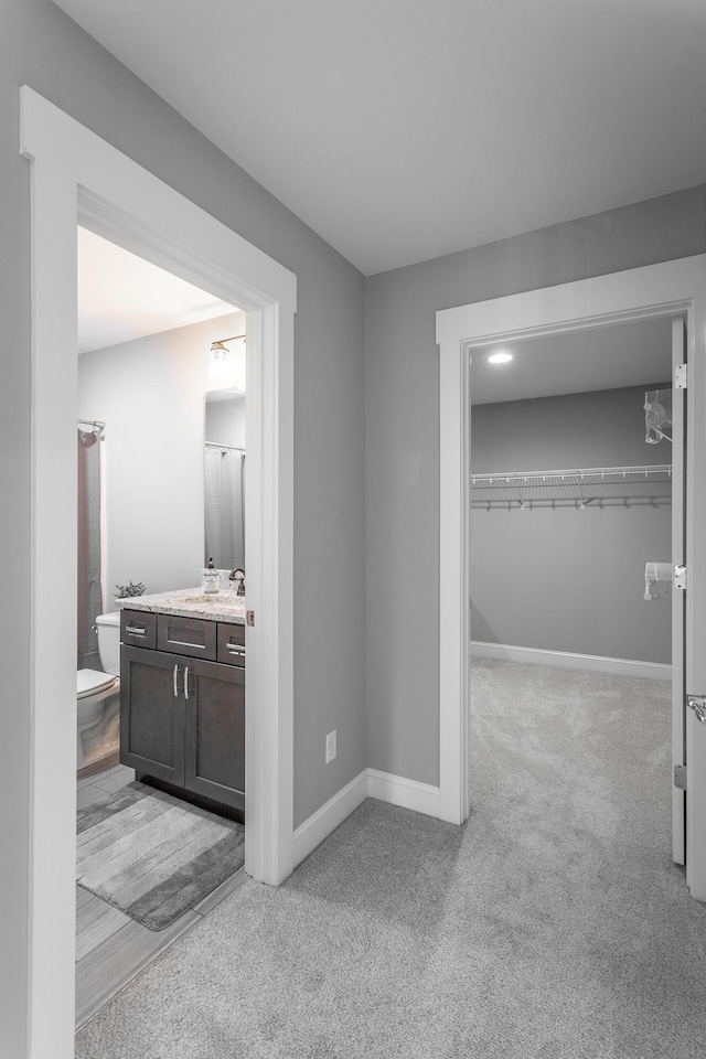 corridor with baseboards, a sink, and light colored carpet
