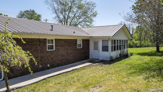 rear view of house featuring a lawn, brick siding, and metal roof