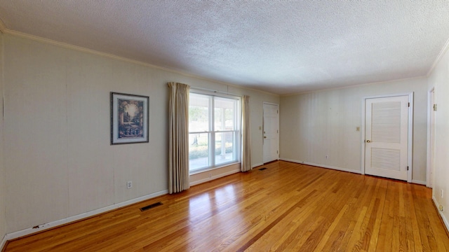 unfurnished room with crown molding, a textured ceiling, light wood-style floors, baseboards, and visible vents
