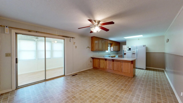 kitchen with a ceiling fan, white refrigerator with ice dispenser, light countertops, a peninsula, and visible vents