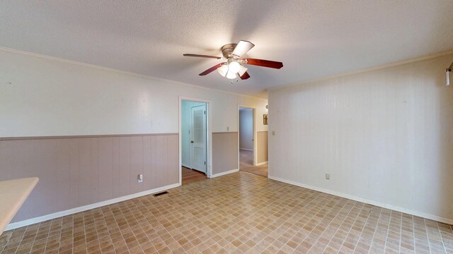 empty room featuring a wainscoted wall, a textured ceiling, visible vents, ceiling fan, and crown molding