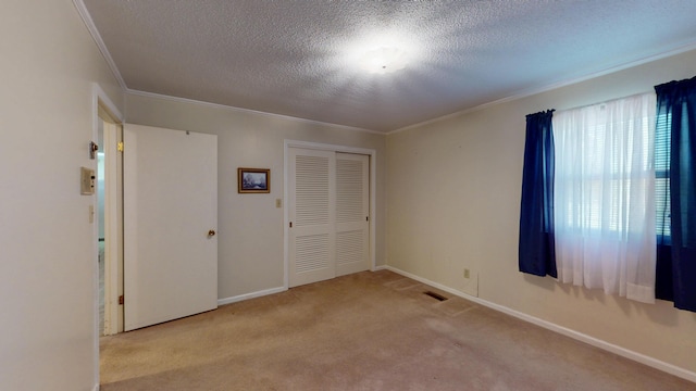 carpeted empty room with a textured ceiling, visible vents, baseboards, and ornamental molding