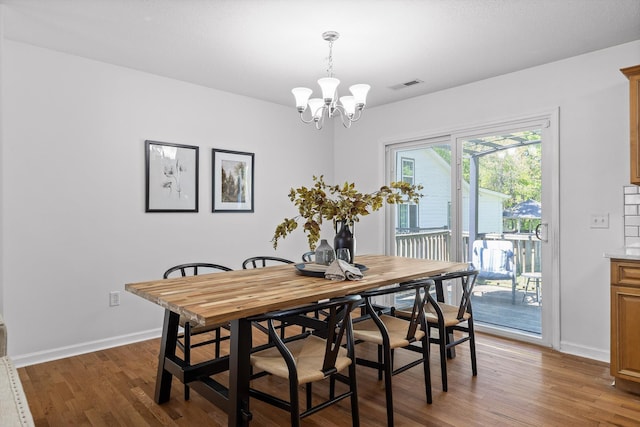 dining area featuring baseboards, visible vents, wood finished floors, and a notable chandelier