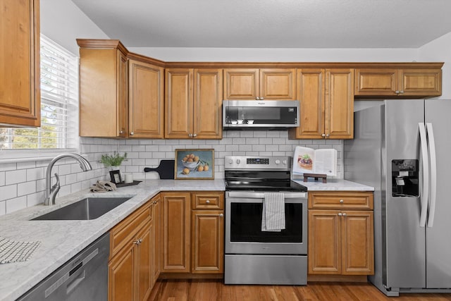 kitchen featuring a sink, appliances with stainless steel finishes, wood finished floors, brown cabinetry, and backsplash