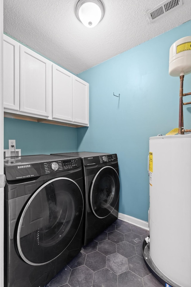 laundry room with a textured ceiling, visible vents, electric water heater, separate washer and dryer, and cabinet space