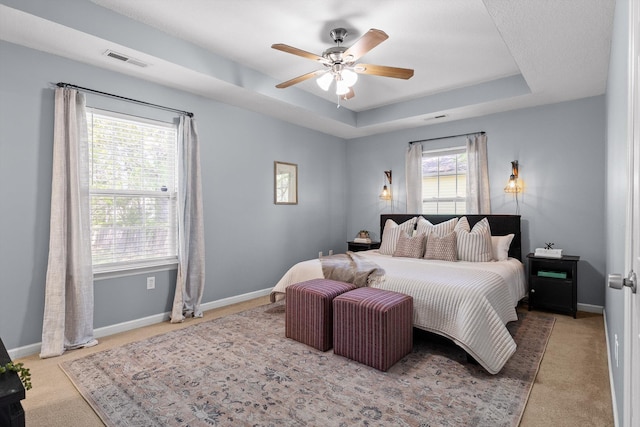 bedroom with a raised ceiling, a ceiling fan, visible vents, carpet, and baseboards