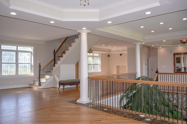 corridor with a tray ceiling, decorative columns, crown molding, baseboards, and recessed lighting