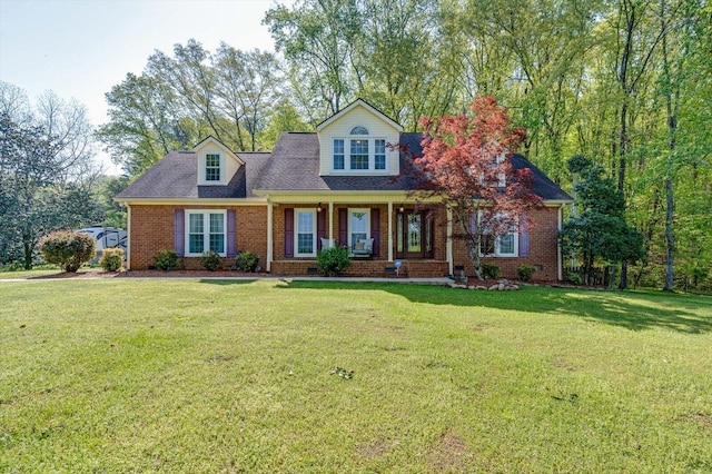 new england style home featuring brick siding, a front lawn, a shingled roof, and a porch