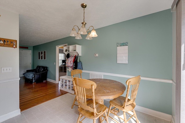 dining space with a chandelier, light wood-style floors, a textured ceiling, and baseboards