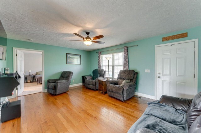 living area featuring light wood-style flooring, a textured ceiling, a ceiling fan, and baseboards