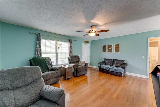 living area with a ceiling fan, baseboards, a textured ceiling, and light wood-style floors