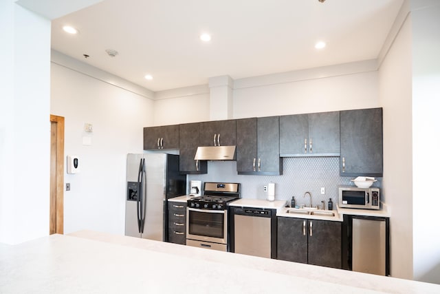 kitchen with recessed lighting, light countertops, under cabinet range hood, a sink, and appliances with stainless steel finishes