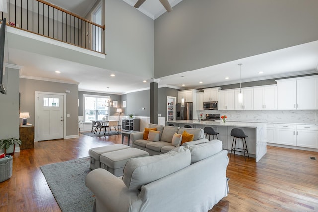 living room with recessed lighting, a towering ceiling, light wood finished floors, ornamental molding, and ornate columns
