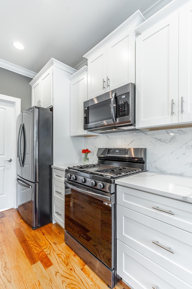 kitchen with white cabinets, stainless steel appliances, tasteful backsplash, light wood-type flooring, and ornamental molding