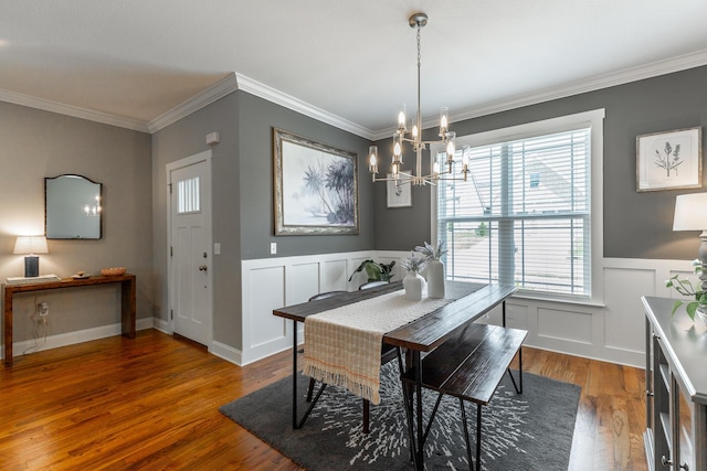 dining space featuring wood finished floors, a decorative wall, ornamental molding, and a notable chandelier