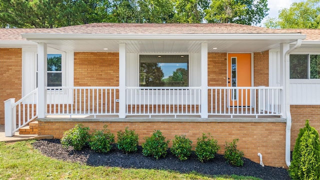 property entrance featuring a porch, roof with shingles, and brick siding