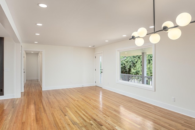 unfurnished living room with light wood finished floors, a notable chandelier, baseboards, and recessed lighting