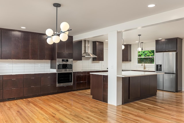 kitchen featuring light wood-type flooring, appliances with stainless steel finishes, wall chimney range hood, and dark brown cabinetry