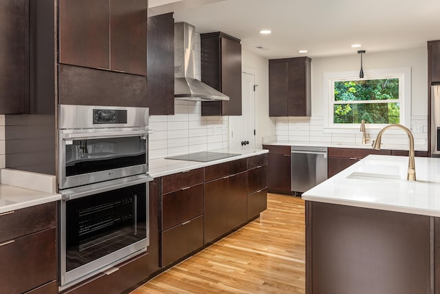 kitchen with wall chimney range hood, stainless steel appliances, light wood-type flooring, and a sink
