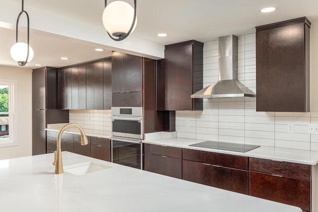 kitchen with a sink, wall chimney range hood, light countertops, double oven, and black electric stovetop