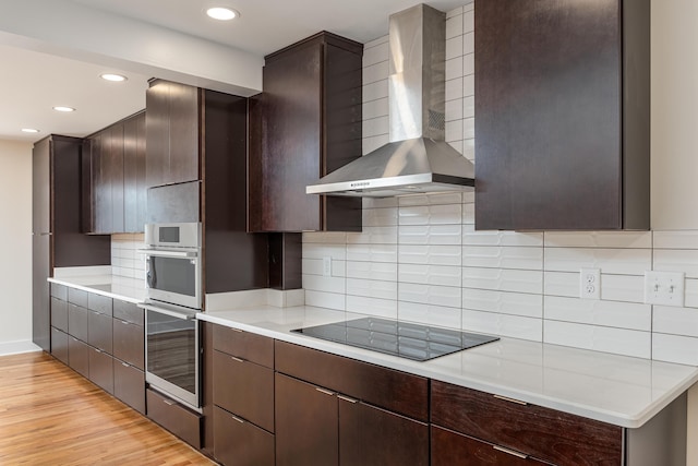 kitchen with wall chimney range hood, light wood finished floors, dark brown cabinetry, and black electric cooktop