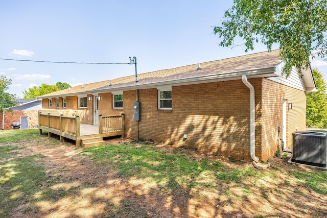 back of property featuring brick siding, a shingled roof, a wooden deck, and central AC
