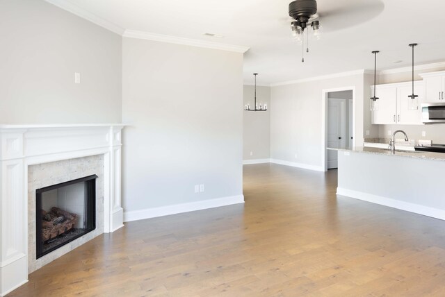 unfurnished living room with baseboards, a fireplace, crown molding, ceiling fan with notable chandelier, and wood finished floors