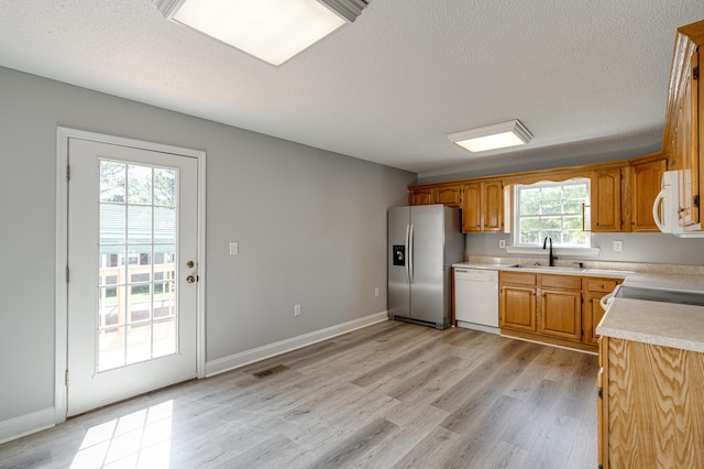 kitchen with a sink, light countertops, white appliances, light wood-style floors, and a textured ceiling