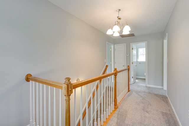 corridor with a notable chandelier, baseboards, light carpet, an upstairs landing, and visible vents