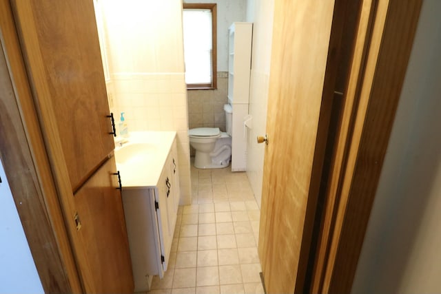 half bathroom featuring tile walls, toilet, vanity, a wainscoted wall, and tile patterned flooring