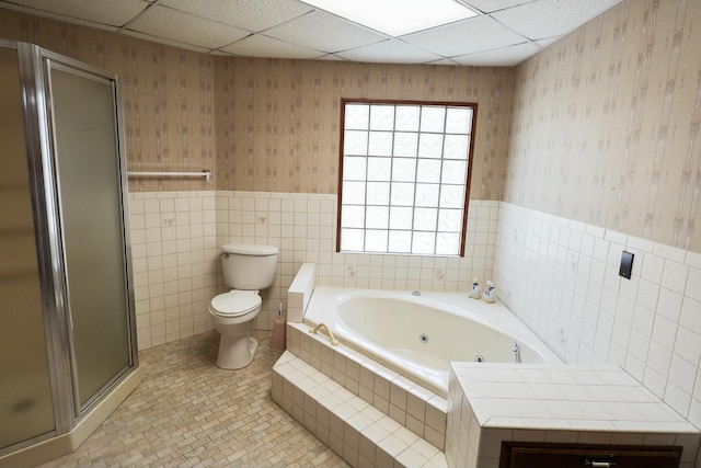 full bathroom featuring a jetted tub, wallpapered walls, a wainscoted wall, toilet, and a shower stall