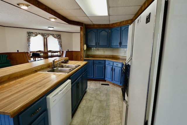 kitchen featuring white appliances, tasteful backsplash, butcher block counters, blue cabinets, and a sink