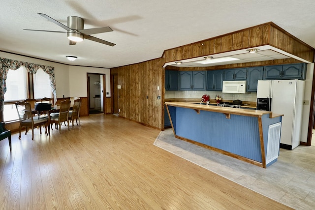 kitchen with ceiling fan, white appliances, blue cabinetry, wooden walls, and a breakfast bar area