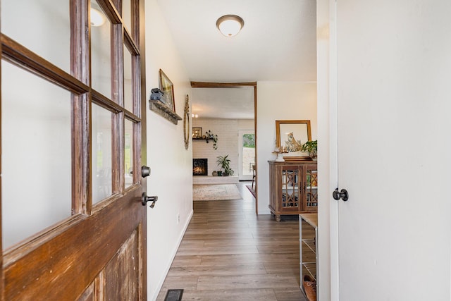 entryway featuring visible vents, baseboards, a brick fireplace, and wood finished floors
