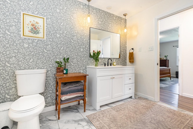 bathroom with vanity, baseboards, toilet, and wallpapered walls