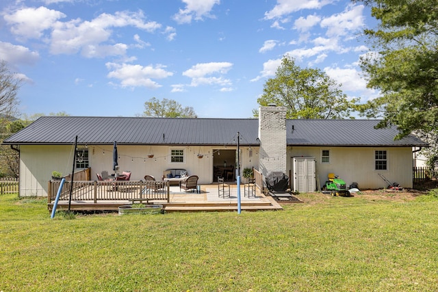 rear view of property featuring fence, a deck, a chimney, metal roof, and a lawn