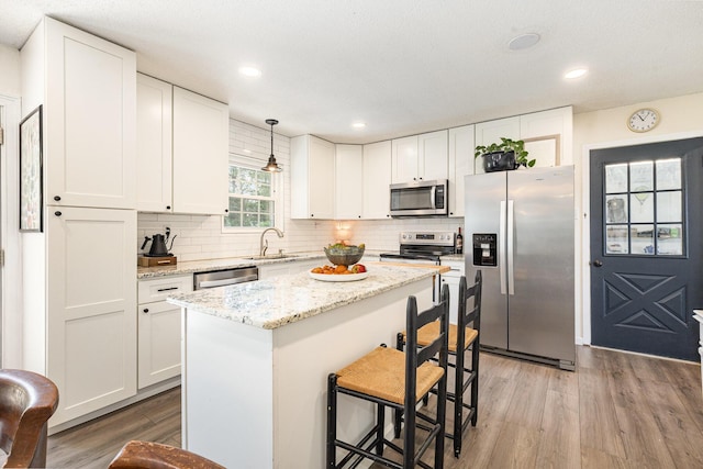 kitchen with appliances with stainless steel finishes, a sink, a breakfast bar area, light wood-type flooring, and tasteful backsplash