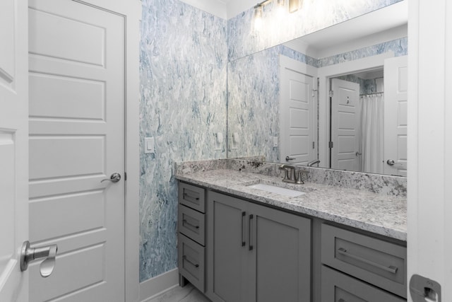 bathroom with vanity, wallpapered walls, and baseboards