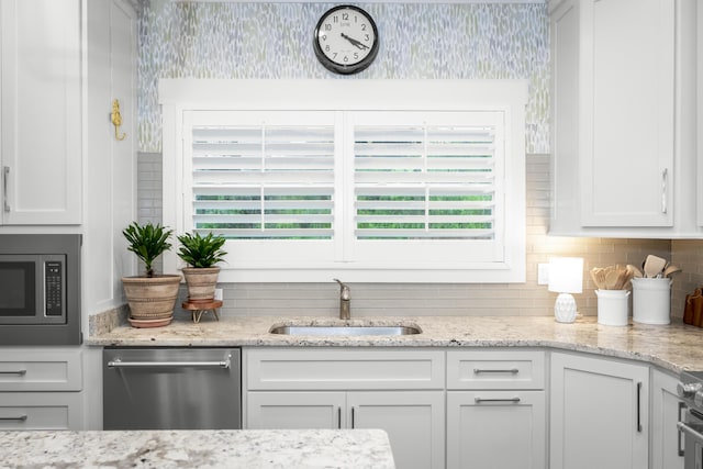 kitchen with a sink, appliances with stainless steel finishes, wallpapered walls, decorative backsplash, and white cabinets
