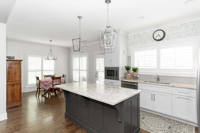 kitchen with stainless steel appliances, a sink, white cabinetry, a kitchen island, and light stone counters